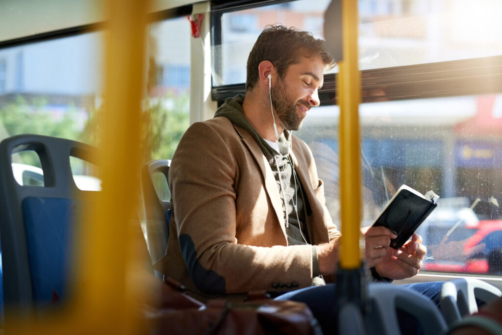 Personne assise dans un bus, lisant un livre tout en écoutant de la musique avec des écouteurs, dans une ambiance calme et détendue